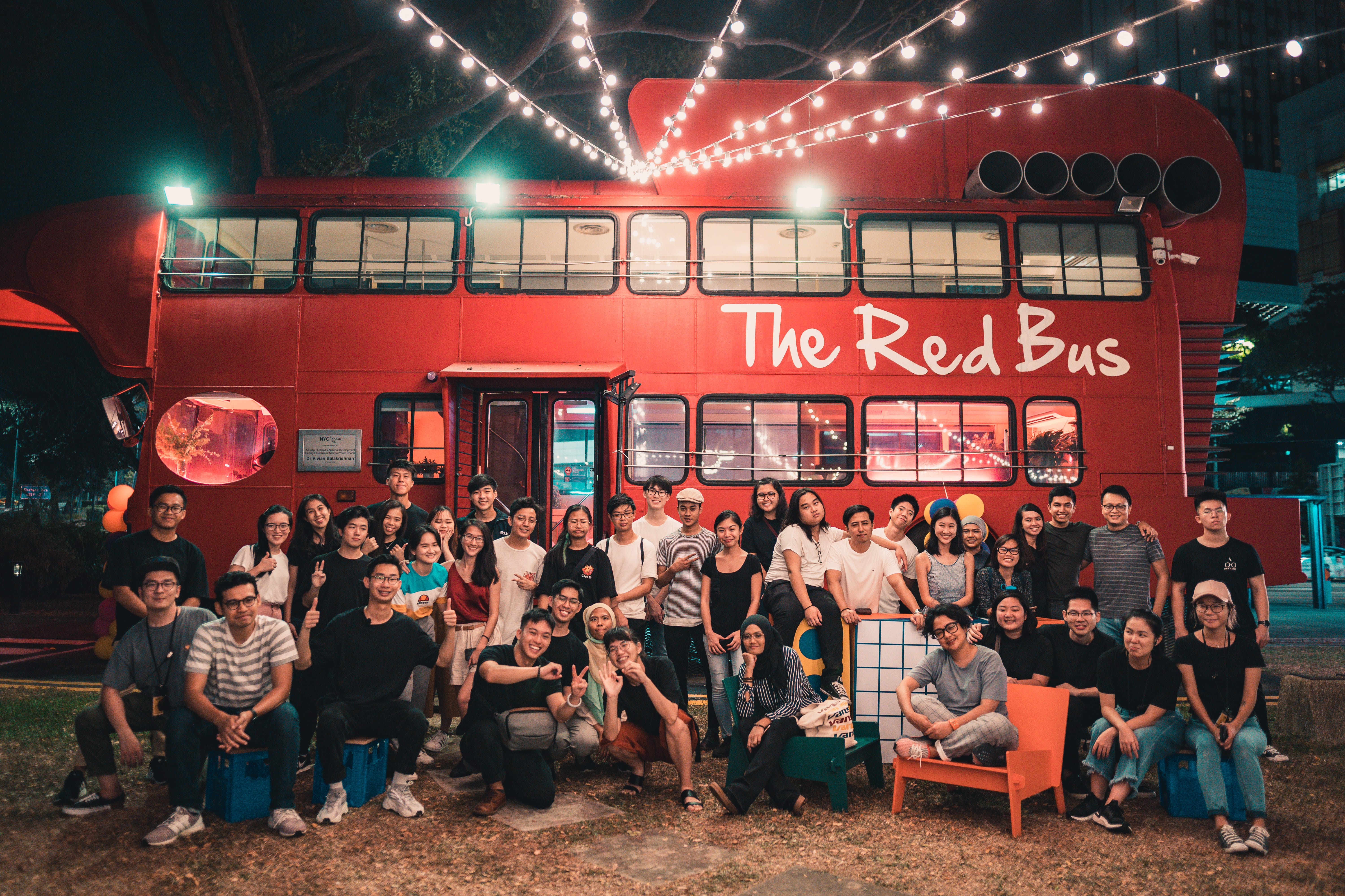 Group of people posing in front of The Red Bus, illuminated by string lights.